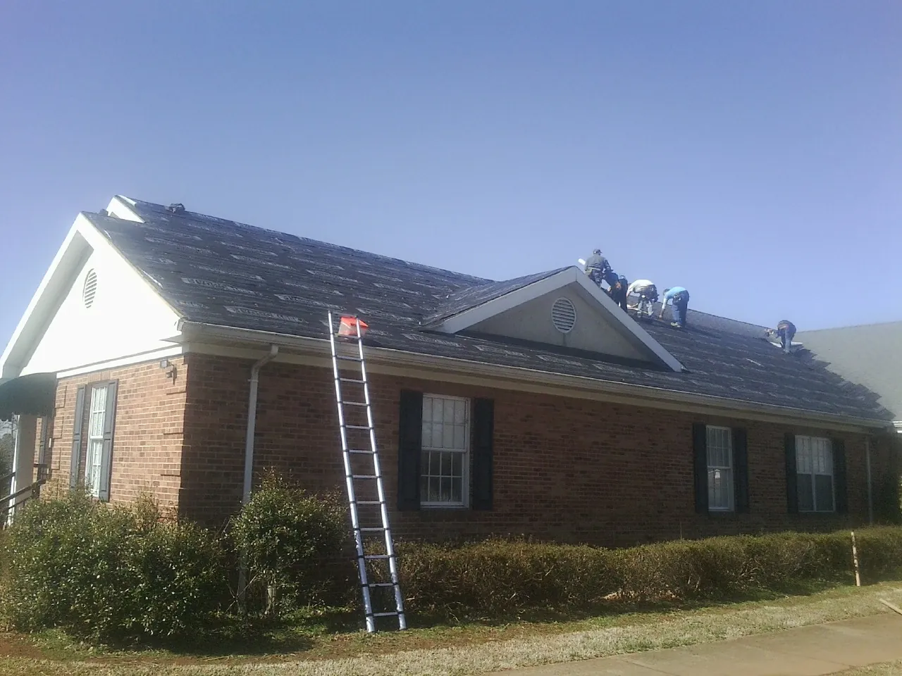 Crew tearing shingles off a brick ranch roof with a ladder set — Emergency Roof Repair work by our crew in Chaplin