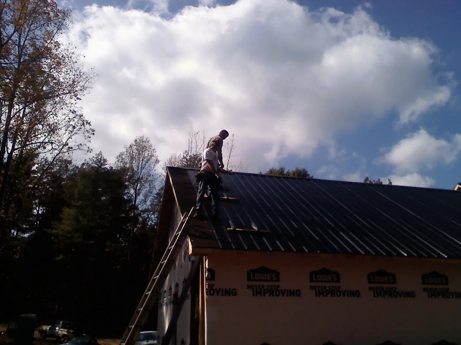 Roofer fastening dark metal panels high against a cloudy sky, from a Roof Inspection job in Chaplin