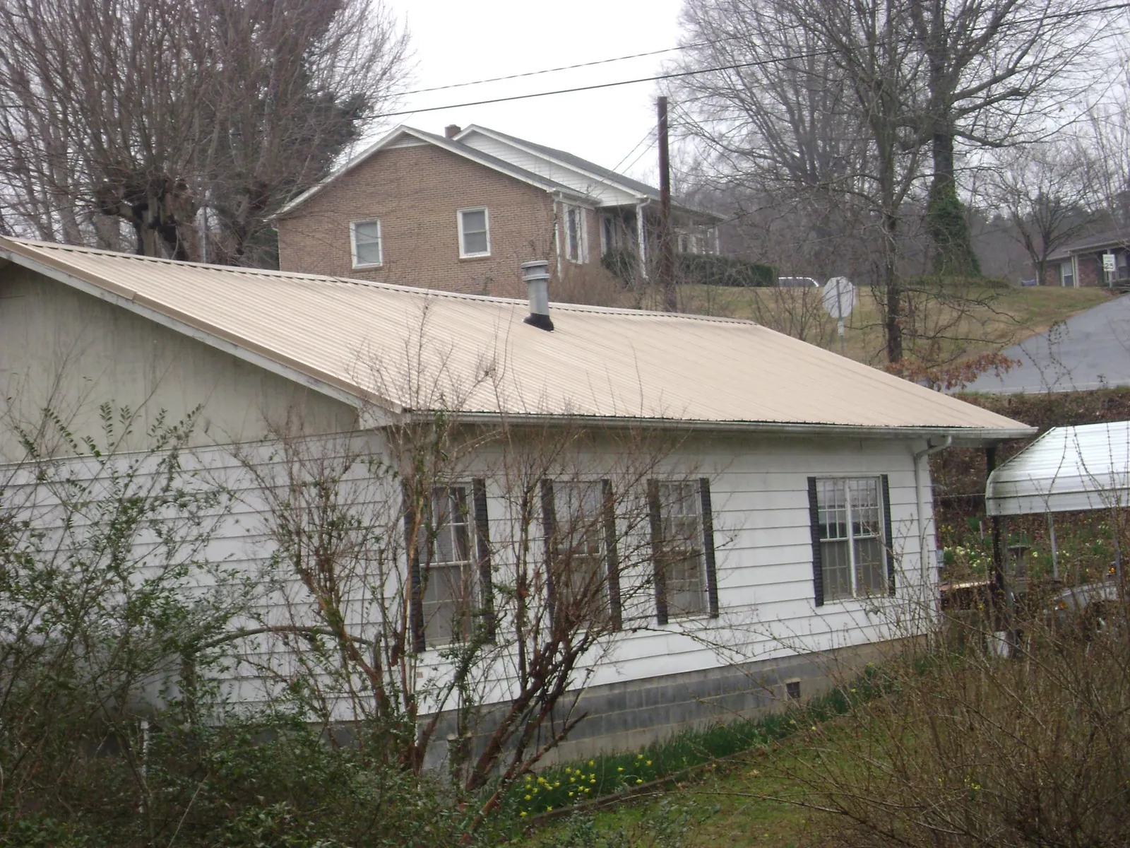 Tan metal roof on a white sided house set into a hillside — Commercial Roofing by Roofing Brothers in Chaplin