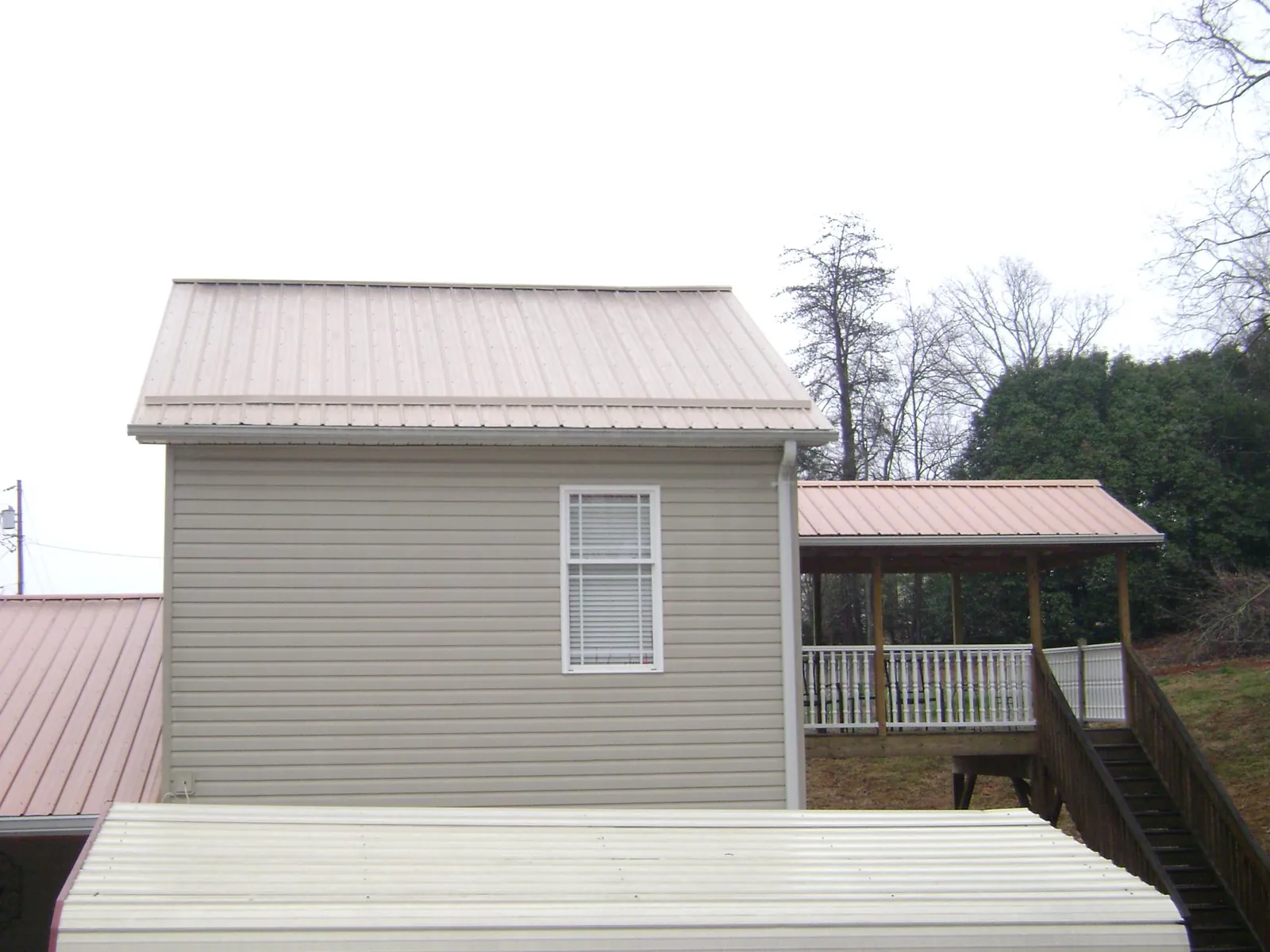 Tan metal roofs on a two story addition and attached porch, from a Roof Replacement job in Chaplin